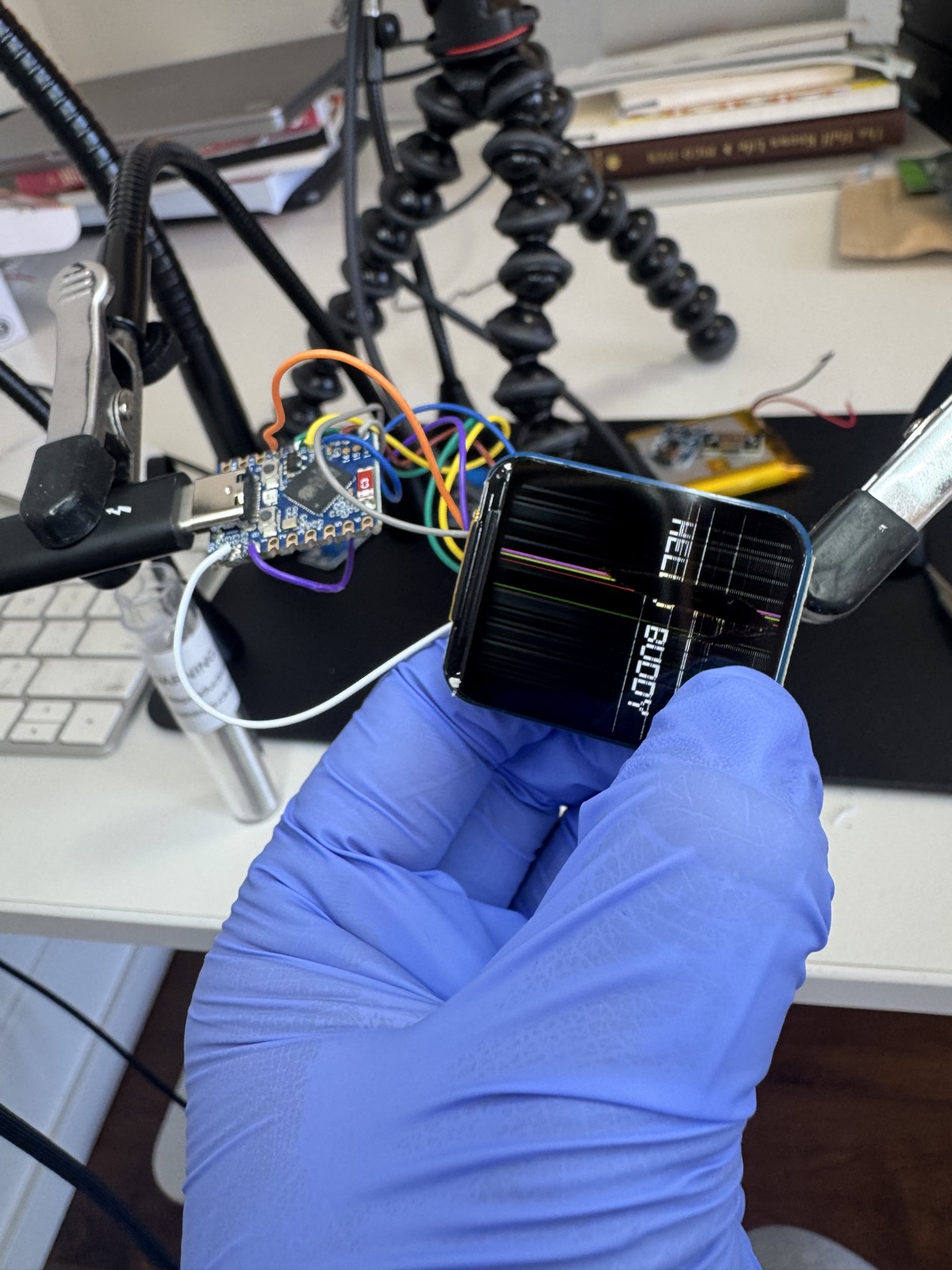 ESP32 board wired to a 1.69-inch LCD module on a black workbench mat with flexible alligator-clip arms holding things in place.